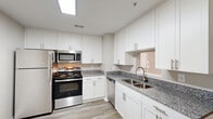 Located at 6719 Cliffdale Rd in Fayetteville, NC, this single-story, one-bedroom, one-bathroom residence offers a thoughtfully designed layout with modern finishes throughout. The kitchen is a standout feature, showcasing crisp white shaker cabinetry, granite countertops, a stainless steel undermount sink, and a full suite of stainless steel appliances including a gas range, built-in microwave, dishwasher, and refrigerator. Light wood-look flooring ties the kitchen together and extends through the main living areas. The open living space flows naturally toward a bright windowed area, allowing generous natural light to fill the room. The bedroom is carpeted for comfort, features a ceiling fan, and includes access to a dedicated closet. A separate laundry room provides washer and dryer hookups along with wire shelving for additional storage. The bathroom offers a full soaking tub and shower combination with brushed nickel fixtures and hardware. Neutral gray walls throughout the home create a clean, versatile backdrop. The overall ambiance is modern, move-in ready, and efficiently designed to make excellent use of the available space.