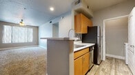 This single-floor residence offers a thoughtfully designed layout that balances comfort and functionality throughout. The kitchen is a standout feature, configured as a galley-style space with warm honey-toned wood cabinetry, light stone countertops, a mosaic tile backsplash, and a full suite of stainless steel appliances including a refrigerator, dishwasher, range, and over-the-range microwave. Wood-look flooring runs through the kitchen, while a peninsula with a built-in sink connects the space to the open living area beyond, which is finished with plush neutral carpeting. The living area is bright and open, with natural light filtering in through vertical-blind-covered windows and a ceiling fan overhead. Multiple bedrooms continue the warm, carpeted aesthetic, each featuring large windows that invite ample natural light and offer outdoor views. Select bedrooms include mirrored sliding closet doors with built-in storage. Two full bathrooms serve the residence, each appointed with a single-sink vanity topped with a stone-look countertop, warm wood cabinetry, a full tub-shower combination with tile surround, and wood-look flooring. Neutral gray walls and clean white trim carry a consistent, modern tone throughout the entire space.