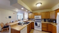Located at 630 Ninth St N in La Crosse, Wisconsin, this single-floor unit offers a well-organized and practical layout designed for comfortable everyday living. The kitchen is a standout feature, equipped with warm oak cabinetry, generous counter space, recessed and flush-mount ceiling lighting, and a full suite of white appliances including an electric range, over-the-range microwave, dishwasher, and refrigerator. The kitchen opens toward the living and dining areas, creating a connected, sociable flow throughout the main living spaces. The living room is bright and welcoming, with large windows that invite natural light and provide views of the surrounding neighborhood. Tile flooring extends through the kitchen and main living areas, offering durability and ease of maintenance. The bedrooms are carpeted for comfort and include windows that allow for additional natural light. The primary bathroom is notably spacious, featuring dual vanities with oak cabinetry, two large mirrors with sconce lighting, tile flooring, and a separate water closet area with a window. A dedicated in-unit laundry area with a full-size washer and dryer and an overhead utility shelf adds practical convenience to this well-appointed unit.