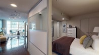 This contemporary single-floor residence showcases a thoughtfully designed open layout with a strong sense of urban sophistication. The highly polished concrete floors run throughout the main living areas, reflecting natural light that pours in through expansive floor-to-ceiling windows, framing impressive city skyline views. Exposed industrial-style ductwork adds a loft-inspired character to the living space, which is anchored by a teal accent wall and a cozy seating area with generous window coverage on two sides.

The kitchen is outfitted with sleek white cabinetry extending to the ceiling, dark granite countertops, a blue-grey subway tile backsplash, and a full suite of stainless steel appliances including a dishwasher, range, built-in microwave, and refrigerator. Track lighting overhead enhances both functionality and ambiance.

The bedroom features a striking black-and-white chevron accent wall, a built-in open closet, and a large floor mirror that amplifies the sense of space. Frosted glass sliding panels elegantly separate the sleeping area from the main corridor. The bathroom carries the teal color palette with bold wall paint, a floating dark-wood vanity, and tile flooring, maintaining a cohesive modern aesthetic throughout the residence.