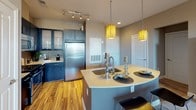 Located at 70 Upper Rock Blvd in Rockville, Maryland, this single-floor residence showcases a well-designed layout with modern finishes throughout. The kitchen is a standout feature, equipped with stainless steel appliances including a gas range, microwave, and refrigerator. Dark cabinetry is complemented by a mosaic tile backsplash, warm hardwood flooring, and a curved kitchen island with a double sink and stylish pendant lighting, making it both functional and visually appealing. The bedrooms are thoughtfully designed, offering plush carpeting and floor-to-ceiling windows that flood the rooms with natural light and provide views of the surrounding greenery and streetscape. The living area continues the theme of abundant natural light, with large sliding glass doors framing outdoor views and creating a bright, inviting atmosphere. The bathrooms are finished with clean tile flooring, dark vanity cabinetry with light countertops, and well-appointed fixtures. One bathroom features a soaking tub with a decorative striped curtain, while another offers direct access to a bedroom. Neutral wall tones and consistent modern detailing tie the entire residence together, creating a cohesive and contemporary living environment in the heart of Rockville.