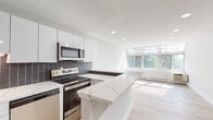 Located at 392 State St in North Haven, Connecticut, this thoughtfully updated single-floor unit combines modern design with functional living. The open-concept kitchen is a standout feature, showcasing glossy white cabinetry, a striking dark mosaic tile backsplash, quartz countertops with a marble-like finish, and a full suite of stainless steel appliances including a dishwasher, range, and over-the-range microwave. A peninsula counter extends the workspace and provides a natural transition into the dining and living areas. The living space is bright and airy, benefiting from a generous bank of windows that invite an abundance of natural light and offer views of surrounding greenery. Light-toned luxury vinyl plank flooring runs throughout the main living areas, lending warmth and a clean, contemporary aesthetic. The bedrooms are carpeted for added comfort and feature recessed lighting and ample closet space. Baseboard heating is present throughout. The bathroom is finished with large-format grey tile surrounding a soaking tub and shower combination, complemented by modern brushed nickel fixtures. Recessed lighting throughout the unit contributes to a bright, polished atmosphere. Clean white walls and crisp trim details unify the space with a cohesive, minimalist character.