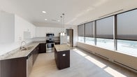 This single-floor space showcases a thoughtfully designed, contemporary interior with a clean, neutral color palette throughout. The open-concept kitchen serves as a central highlight, featuring a large granite-topped island with dark espresso cabinetry below, complemented by crisp white upper cabinets extending to the ceiling. Stainless steel appliances, including a refrigerator, range, microwave, and dishwasher, provide a polished, functional aesthetic. Pendant lighting over the island adds refined detail, while recessed lighting illuminates the space evenly. Light wood-look tile flooring flows seamlessly from the kitchen into the living area.

The living area is distinguished by a dramatic wall of floor-to-ceiling windows fitted with roller shades, offering sweeping views of the surrounding cityscape and filling the space with generous natural light. Baseboard heating runs along the window line, providing efficient climate control.

The bedrooms are carpeted for comfort, finished in soft neutral tones, and equipped with baseboard heating. The bathrooms feature dark-toned vanities with light countertops, large mirrors, and full soaking tub and shower combinations with built-in shelving, delivering a clean and functional design throughout.