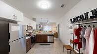 Located at 1223 N Haven Dr in Fayetteville, Arkansas, this single-story residence offers four bedrooms and four bathrooms within a thoughtfully designed layout. The open-concept kitchen and living area serves as the heart of the home, featuring stainless steel appliances, two-tone cabinetry with white upper cabinets and warm wood lower cabinets, a peninsula with a sink, and light wood-style flooring. The living area extends naturally from the kitchen, highlighted by a ceiling fan and a sliding glass door that opens to a private balcony with lush outdoor views. Each bedroom is carpeted and receives ample natural light through large windows with blinds and curtains. Several bedrooms include built-in shelving units above the headboard area, providing functional storage and display space. Each bedroom is paired with its own private bathroom finished with wood-look tile flooring, a vanity with granite-style countertops, and access to a dedicated walk-in closet. The closets are generously proportioned with hanging rod storage. Additional features include two hallways connecting the private rooms, a dedicated laundry room, and five closets throughout. The neutral color palette and modern finishes create a clean, cohesive aesthetic throughout the entire residence.