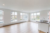 This well-appointed 3-bedroom, 2-bathroom single-floor residence offers a clean, modern aesthetic defined by crisp white walls, light hardwood flooring, and an abundance of natural light. The open-concept living, dining, and kitchen area serves as the heart of the home, featuring expansive multi-pane windows along multiple walls that frame views of the surrounding urban neighborhood. The kitchen is equipped with white shaker cabinetry, dark granite-style countertops, stainless steel appliances including an electric range, built-in microwave, and dishwasher, alongside a peninsula that connects seamlessly to the living and dining areas. The generously sized primary bedroom includes multiple closets and connects to adjacent rooms via a well-organized hallway. The additional bedrooms are bright and functional, each with windows overlooking the exterior and dedicated closet space. Both bathrooms feature white vanities with large mirrors, modern fixtures, and hardwood flooring. The residence also includes a dedicated laundry area and an impressive eight closets distributed throughout, offering exceptional storage. Baseboard heating is present throughout, and recessed lighting adds to the clean, contemporary feel of the space.