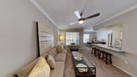 This single-floor residence offers a thoughtfully designed layout that balances comfort and functionality. The open-concept living area is finished with plush carpeting, crown molding, and a ceiling fan, creating a welcoming atmosphere. Large windows with plantation-style blinds flood the space with natural light and provide views of the outdoors. A glass-top coffee table and generous seating anchor the living room, which flows seamlessly into the dining and kitchen areas.

The kitchen is well-equipped and features crisp white cabinetry, granite countertops, a subway tile backsplash, hardwood-style flooring, and stainless steel appliances including a refrigerator, range, and built-in microwave. A peninsula with bar seating connects the kitchen to the adjacent dining space, making it ideal for both casual meals and entertaining.

The bedroom is a serene retreat, complete with carpet flooring, a ceiling fan, a dedicated workspace, and direct access to an outdoor area through sliding glass doors. The en-suite bathroom is elegantly finished with granite countertops, white cabinetry, a large vanity mirror, and hardwood-style flooring, complemented by a tiled tub-and-shower combination. Throughout the residence, a cohesive neutral color palette and consistent finishes create a polished, harmonious environment.