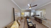 This single-floor residence offers a thoughtfully designed layout that balances comfort and functionality. The open-concept living area is finished with plush carpeting, crown molding, and a ceiling fan, creating a welcoming atmosphere. Large windows with plantation-style blinds flood the space with natural light and provide views of the outdoors. A glass-top coffee table and generous seating anchor the living room, which flows seamlessly into the dining and kitchen areas.

The kitchen is well-equipped and features crisp white cabinetry, granite countertops, a subway tile backsplash, hardwood-style flooring, and stainless steel appliances including a refrigerator, range, and built-in microwave. A peninsula with bar seating connects the kitchen to the adjacent dining space, making it ideal for both casual meals and entertaining.

The bedroom is a serene retreat, complete with carpet flooring, a ceiling fan, a dedicated workspace, and direct access to an outdoor area through sliding glass doors. The en-suite bathroom is elegantly finished with granite countertops, white cabinetry, a large vanity mirror, and hardwood-style flooring, complemented by a tiled tub-and-shower combination. Throughout the residence, a cohesive neutral color palette and consistent finishes create a polished, harmonious environment.