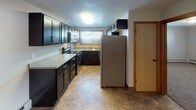 This single-floor unit offers a practical and well-organized layout across its main living spaces. The living room is a generously proportioned area finished with dark hardwood-style plank flooring, neutral-toned walls, a textured ceiling, and a wide window fitted with vertical blinds that allows natural light to fill the space. A wall-mounted HVAC unit and baseboard heating provide climate control. The room opens directly into the kitchen, creating a connected flow between living and dining areas.

The kitchen is well-equipped and features an abundance of dark cabinetry that extends along two walls, offering substantial storage. Light countertops provide a clean contrast against the dark cabinets, and appliances include a stainless steel refrigerator, electric range, and built-in microwave. Tile flooring completes the kitchen's functional aesthetic, and a window above the sink introduces additional natural light.

The bedroom is a comfortable, quiet space with plush carpeting, neutral walls, baseboard heating, and a window with blinds. The full bathroom is elongated and thoughtfully designed, featuring a wide double vanity with dark cabinetry, a white countertop, tile flooring, and baseboard heating, providing both style and practicality.