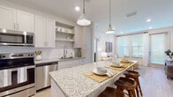 This single-floor residence offers a cohesive, modern design characterized by a neutral palette, light wood-style flooring, and an abundance of natural light throughout. The open-concept kitchen serves as a central highlight, featuring white shaker cabinetry, subway tile backsplash, granite countertops, and a generously sized island with bar seating illuminated by pendant lighting. Stainless steel appliances, including a side-by-side refrigerator, range, and microwave, complete the well-appointed cooking space. The kitchen flows seamlessly into the living area, which benefits from large windows dressed with light-filtering blinds and sheer curtains, creating a bright and welcoming atmosphere.

The residence includes two bedrooms, each carpeted and filled with natural light. The primary bedroom connects to an en-suite bathroom with granite vanity counters, white shaker cabinetry, a tiled shower, and direct access to a spacious walk-in closet with wire shelving systems. A second full bathroom mirrors the same finishes, offering a tub-shower combination and an adjacent walk-in closet. Throughout, the design maintains a clean, contemporary feel with consistent finishes and thoughtful storage solutions.
