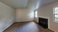 Located at Vineyards Lane in Bremerton, Washington, this single-floor unit offers a functional and comfortable layout throughout. A carpeted hallway leads into the main living area, where a vaulted ceiling adds a sense of openness. The living room is anchored by a fireplace with a classic white surround and dark hearth, complemented by a window framing views of surrounding greenery. A sliding glass door opens directly onto a private deck, extending the living space outdoors and providing pleasant tree-lined views.

The galley-style kitchen is efficiently designed with white cabinetry, light countertops, tile flooring, and black appliances including a range and refrigerator. A peninsula counter with breakfast bar seating connects the kitchen to the adjacent living and dining area. In-unit laundry is conveniently located just off the kitchen.

The bedrooms are carpeted and well-lit with windows overlooking the exterior. One bedroom features an adjoining hallway that leads to a full bathroom complete with a tub/shower combination. Additional closet space is accessible throughout the unit. The overall layout is practical and cohesive, with neutral tones and soft carpet creating a warm, livable atmosphere throughout.