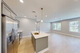 This well-appointed one-bedroom, one-bathroom unit at 12 Station Street in Middleborough, Massachusetts offers a thoughtfully designed layout with modern finishes throughout. The open-concept kitchen and living area serves as the heart of the home, anchored by a striking blue kitchen island with a white quartz countertop and pendant lighting overhead. Gray shaker-style cabinetry, stainless steel appliances, and light hardwood flooring complete the kitchen's contemporary aesthetic. The living area benefits from recessed lighting and sliding glass doors that open onto a private outdoor deck, filling the space with natural light and providing seamless indoor-outdoor access. The bedroom is a comfortable retreat featuring plush carpet, multiple windows with slatted blinds that invite abundant natural light, and recessed ceiling lighting. A dedicated closet provides practical storage. The full bathroom is finished with large-format neutral tile surrounding a soaking tub and shower combination, complemented by tile flooring and a window for natural light. Neutral, soft-toned walls throughout the unit create a clean, cohesive ambiance that is both calm and move-in ready. The unit also includes a separate room with hardwood flooring, suitable for use as a home office or flex space.