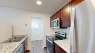 This two-bedroom, two-bathroom single-floor residence at 1655 S Ingram Mill Rd in Springfield, Missouri offers a practical and well-appointed layout. Wood-look plank flooring runs throughout the unit, creating a cohesive and easy-to-maintain aesthetic across every room.

The kitchen is a standout feature, equipped with rich dark-wood cabinetry, light granite-style countertops, and a full suite of stainless steel appliances including an electric range, built-in microwave, dishwasher, and refrigerator. A double-basin sink and natural light from a window make the kitchen both functional and inviting.

The open living area flows naturally from the kitchen through an arched passageway, providing a clean, unobstructed space for everyday living. A hallway connects the main living areas to the two bedrooms and two closets, offering efficient use of the floor plan.

The spacious primary bedroom provides a generous footprint with natural light from a window, while the second bedroom is equally well-lit and versatile. Both rooms feature the same wood-look flooring and bright white walls found throughout the unit.

The bathrooms include a tub-shower combination with white surround, complemented by matching granite-style vanity countertops and consistent finishes. The overall ambiance is clean, neutral, and move-in ready.