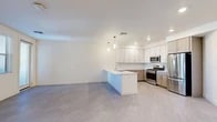 Located at 8901 Holly Ave NE in Albuquerque, New Mexico, this thoughtfully designed one-bedroom, one-bathroom residence offers a clean, contemporary aesthetic throughout its single-floor layout. The open-concept living area seamlessly connects the dining room, kitchen, and living room into a bright, cohesive space bathed in natural light. The kitchen is a standout feature, equipped with stainless steel appliances—including a gas range, microwave, and French door refrigerator—complemented by two-tone cabinetry in white and warm wood tones, a subway tile backsplash, quartz countertops, and a large center island with a built-in sink and pendant lighting above. Light wood-look flooring flows consistently throughout the entire residence. The spacious bedroom offers a ceiling fan, a window with natural views, and direct access to a generous walk-in closet with built-in shelving. The full bathroom features a wood-toned vanity with a double sink, quartz countertops, a soaking tub with tiled surround, and a framed mirror. Additional conveniences include an in-unit laundry area and a private patio, rounding out a well-appointed and functional living space.