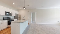 Located at 484 Greenmont Dr in Lewis Center, Ohio, this single-floor home offers a clean, modern design with a neutral color palette throughout. The open-concept kitchen is a standout feature, showcasing white shaker-style cabinetry with brushed gold hardware, granite countertops, a center island with a undermount sink, stainless steel appliances including a refrigerator, electric range, and over-the-range microwave, and warm hardwood-style flooring. Pendant lighting above the island adds a polished touch. The kitchen flows seamlessly into the living area, which is finished with plush carpeting and a large window that fills the space with natural light and provides views of the surrounding greenery. A door leads to an outdoor area, enhancing the connection to the exterior. The bedrooms are generously sized, carpeted, and include ceiling fans and closets with built-in shelving. The bathrooms feature the same granite countertops and white cabinetry found in the kitchen, warm hardwood-style flooring, and a walk-in glass-door shower in the primary bath, which also connects to a spacious walk-in closet. The overall ambiance is bright, clean, and move-in ready.