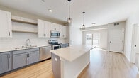 Located at 13972 Edgewood Ave in Savage, MN, this well-designed 2-bedroom, 2-bathroom residence offers a clean, contemporary aesthetic throughout its efficiently arranged single-floor layout. The kitchen serves as the centerpiece of the home, showcasing a striking two-tone design with crisp white upper cabinetry and soft gray lower cabinets, a classic subway tile backsplash, light quartz countertops, and a full suite of stainless steel appliances. A generously sized central island with pendant lighting provides additional prep space and casual seating, flowing seamlessly into the open living area, which is brightened by a sliding glass door leading to a private balcony. The bathrooms are finished with white shaker-style vanities, black hardware accents, and light wood-look flooring. One bathroom features a soaking tub and shower combination, while the other includes a dedicated walk-in shower. The primary bedroom offers comfortable carpeting, a window with natural light, and access to a spacious walk-in closet with wire shelving systems for organized storage. The second bedroom is equally well-lit with its own window. Light wood-look flooring runs through the main living areas, tying together the bright, neutral palette that defines the overall ambiance of this move-in-ready home.
