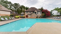 Located at 3400 Kimball Bridge Rd in Alpharetta, Georgia, this outdoor pool area serves as a standout community amenity designed for relaxation and recreation. The generously sized swimming pool features clear, blue water and is framed by a wide concrete sundeck that offers ample space for lounging. Rows of reclining lounge chairs are arranged along multiple sides of the pool, providing plenty of seating for residents and guests. Shaded seating options, including umbrella-covered tables and chairs, offer comfortable alternatives for those seeking refuge from the sun.

The pool area is enclosed by a wrought iron fence, ensuring both safety and a sense of privacy. A pergola structure on one side of the deck adds architectural charm and additional shaded gathering space. Mature trees and well-maintained greenery surround the perimeter, creating a serene, natural backdrop that enhances the outdoor atmosphere. A brick building with traditional architectural details is visible adjacent to the pool, complementing the overall aesthetic of the community.

The space is thoughtfully landscaped, with flowering trees and shrubs adding vibrant color throughout the season. Whether used for active swimming or leisurely sunbathing, this outdoor pool area provides a welcoming and functional retreat within the Alpharetta community.