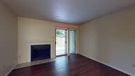 Located at 10610 Morado Cir in Austin, Texas, this single-story home offers a practical and comfortable layout with consistent design details throughout. The living area is a standout space, featuring rich dark hardwood flooring, a classic fireplace with a tiled hearth and white mantel, and a sliding glass door that fills the room with natural light while providing direct access to the outdoors and views of surrounding greenery. The galley-style kitchen is efficiently designed with dark cabinetry, dark countertops, black appliances including a refrigerator, range, and microwave, and track lighting overhead. Hardwood flooring continues into the kitchen, adding warmth and continuity. A bar-height counter separates the kitchen from an adjacent dining or flex area, which connects to a hallway leading further into the home. The bedroom is carpeted for comfort and features a ceiling fan with light fixture and a window with blinds allowing for natural light and privacy. The bathroom includes a full tub and shower combination with white tile surround, hardwood flooring, and clean, functional fixtures. Overall, the home presents a cohesive aesthetic with neutral wall tones, warm wood flooring, and practical amenities throughout.