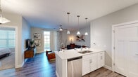 This thoughtfully designed single-floor residence offers a seamless open-concept layout that connects the kitchen, dining, and living areas into one cohesive, light-filled space. The kitchen is a standout feature, showcasing white shaker cabinetry, quartz countertops, a large center island with a double-basin sink and bar seating, and a full suite of stainless steel appliances, including a refrigerator, microwave, and dishwasher. A tile backsplash and pendant lighting add refined detail to the space. The kitchen flows naturally into a dedicated dining area and an open living room, where wood-style flooring, a ceiling fan, and a glass door leading to an outdoor area contribute to an airy, welcoming atmosphere. A closet pantry provides additional storage near the kitchen. The living room accommodates a comfortable seating arrangement and is bathed in natural light from large windows. The bedroom offers plush carpeting, ample closet space, and a serene, neutral palette. The bathroom features a tub-shower combination with floor-to-ceiling tile surround, a white vanity with quartz countertop, and wood-style flooring. Soft, neutral tones and modern finishes are carried consistently throughout, creating a polished and cohesive interior.
