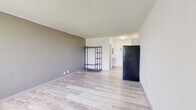 Located at 1057 Broward Rd in Jacksonville, FL, this single-floor studio unit offers an efficient, open-concept layout that combines the living and kitchen areas into one cohesive space. Light wood-style laminate flooring runs throughout, giving the interior a clean and cohesive look. The living area is bright and open, anchored by a large window fitted with vertical blinds that frames outdoor views of surrounding greenery, including palm trees — a nod to the Florida setting. A wall-mounted HVAC unit provides climate control directly in the living space. The kitchen area is tucked neatly at one end of the unit, featuring white cabinetry, granite-style countertops, and stainless steel appliances including a full-size refrigerator and microwave. Textured walls and a textured ceiling add subtle character throughout. The bathroom is a standout feature, finished with large-format marble-look tile on both the floor and the tub surround, creating an elegant contrast to the otherwise minimal aesthetic. A combination tub and shower completes the bathroom. Track lighting in the kitchen area and soft ambient lighting throughout ensure the space is well-lit. Overall, the unit presents a functional and tidy living environment suitable for single occupancy.