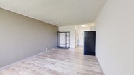 Located at 1057 Broward Rd in Jacksonville, FL, this single-floor studio unit offers an efficient, open-concept layout that combines the living and kitchen areas into one cohesive space. Light wood-style laminate flooring runs throughout, giving the interior a clean and cohesive look. The living area is bright and open, anchored by a large window fitted with vertical blinds that frames outdoor views of surrounding greenery, including palm trees — a nod to the Florida setting. A wall-mounted HVAC unit provides climate control directly in the living space. The kitchen area is tucked neatly at one end of the unit, featuring white cabinetry, granite-style countertops, and stainless steel appliances including a full-size refrigerator and microwave. Textured walls and a textured ceiling add subtle character throughout. The bathroom is a standout feature, finished with large-format marble-look tile on both the floor and the tub surround, creating an elegant contrast to the otherwise minimal aesthetic. A combination tub and shower completes the bathroom. Track lighting in the kitchen area and soft ambient lighting throughout ensure the space is well-lit. Overall, the unit presents a functional and tidy living environment suitable for single occupancy.