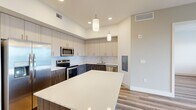 Located in Stuart, FL, this thoughtfully designed 5-bedroom, 2-bathroom unit offers a contemporary aesthetic throughout its single-floor layout. The open-concept kitchen is a standout, showcasing a two-tone cabinetry scheme with light upper cabinets and rich walnut-toned lower cabinets, a marble-style tile backsplash, a large center island with a crisp white quartz countertop, and a full suite of stainless steel appliances including a refrigerator, range, microwave, and dishwasher. Pendant lighting above the island adds a refined touch. The kitchen flows seamlessly into the living area, where light wood-look flooring, recessed lighting, and a ceiling fan create a bright, airy atmosphere. Sliding glass doors lead to a private balcony with open views of the surrounding landscape. The five bedrooms are well-proportioned, each featuring the same wood-look flooring and large windows that bring in ample natural light. The two bathrooms are finished with large-format tile flooring, dual-sink vanities with walnut cabinetry and white countertops, frameless glass shower enclosures, and modern fixtures. A hallway and closet complete the functional layout, making this unit well-suited for shared or family living in the heart of Stuart.