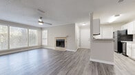 This one-bedroom, one-bathroom unit in Hoover, Alabama offers a well-appointed single-floor layout designed for comfortable everyday living. The open living area is a standout, featuring gray luxury vinyl plank flooring that flows throughout the main space, crown molding, a textured ceiling, and a ceiling fan with integrated lighting. A tile-surround wood-burning fireplace serves as the focal point of the living room, adding warmth and character to the neutral, light-toned interior. Multiple windows fitted with horizontal blinds allow natural light to fill the space while maintaining privacy. An adjacent area extends the living space further, with a glass-paned exterior door providing additional access and outdoor views. The galley-style kitchen is efficiently designed with white shaker-style cabinetry, light granite-look countertops, gray LVP flooring, and black appliances including a range, microwave, and dishwasher, along with a stainless steel sink. The bedroom offers a quieter retreat, finished with plush wall-to-wall carpet, a ceiling fan, and a natural light-admitting window. The overall aesthetic is clean, modern, and neutral throughout, making this a practical and inviting space located in Hoover, AL.