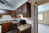 This single-floor, 3-bedroom, 1-bathroom unit offers a practical and well-organized layout. The kitchen is a functional highlight, featuring rich dark wood cabinetry, granite-style laminate countertops, and a full suite of stainless steel appliances including a refrigerator, dishwasher, and electric range. A ceiling fan overhead and wood-look vinyl flooring complete the kitchen's clean, utilitarian aesthetic. Adjacent to the kitchen, an entry area with matching wood-tone doors provides a natural transition throughout the space.

The bedrooms are carpeted and finished with warm beige walls and wood-trimmed baseboards and door frames. The primary bedroom is the most spacious of the three, featuring two windows that invite natural light and views of surrounding greenery, along with a wall-mounted AC unit and baseboard heating. The additional bedrooms are similarly carpeted, with one featuring a sliding wood-panel closet door with a hanging rod for storage.

The bathroom is clean and simply appointed, with a modern white vanity countertop, an integrated sink, wood-framed mirror, and pendant lighting. The hallway connects the rooms efficiently, and a dedicated closet provides additional storage. Baseboard heating is present throughout, ensuring year-round comfort in this cozy, efficiently designed home.