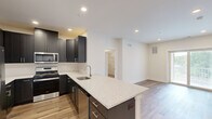 Located in Skillman, NJ, this well-appointed single-floor residence offers three bedrooms, two bathrooms, and a smartly designed layout that maximizes functionality and comfort. The modern kitchen is a standout feature, showcasing dark shaker-style cabinetry, granite-look countertops, a central island with a built-in sink, and a full suite of stainless steel appliances including a gas range, microwave, and refrigerator with ice maker. Light wood-look flooring flows throughout the main living areas, complementing the clean white walls and recessed lighting overhead. The open-concept design connects the kitchen seamlessly to the living room, which features sliding glass doors leading to a private balcony. The spacious primary bedroom includes a walk-in closet with built-in wire shelving, while additional bedrooms offer plush carpeting and ample natural light. Both bathrooms are finished with dark vanity cabinetry, white countertops, and tile flooring; one features a tub-shower combination with white subway tile surround. A dedicated utility room and hallway complete the layout. The overall aesthetic is contemporary and move-in ready, with neutral tones and quality finishes throughout.