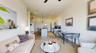 This thoughtfully designed one-bedroom, one-bathroom residence offers a bright and modern open-concept floor plan with light wood-style flooring throughout. The living area is anchored by large French doors that open to a private balcony, flooding the space with natural light and providing views of the surrounding neighborhood. A ceiling fan overhead and clean white walls contribute to the airy, contemporary atmosphere.

The kitchen is a standout feature, boasting white shaker cabinetry extending to the ceiling, dark quartz countertops, a subway tile backsplash, stainless steel appliances including a side-by-side refrigerator, and a central island with pendant lighting and bar seating — ideal for both cooking and casual dining. A dedicated dining area sits adjacent to the kitchen.

The bedroom is a serene retreat with soft neutral tones, wood-style flooring, and access to a well-organized walk-in closet with built-in shelving and hanging rods. The bathroom features a dual-sink vanity with backlit mirrors, matte black fixtures, white quartz countertops, and a glass-enclosed walk-in shower. Additional conveniences include a laundry area and a utility room. Hallways connect the spaces efficiently, completing this polished and functional single-floor residence.