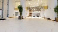 Panorama Tower's lobby is an architecturally striking entry space designed to impress. The floor is clad in expansive white marble-style tile with subtle gold veining, lending the space a refined, luxurious quality that flows seamlessly throughout. Soaring double-height ceilings amplify the sense of grandeur, while floor-to-ceiling glass walls and entry doors flood the interior with abundant natural light, offering clear views to the surrounding streetscape.

Sheer, floor-length drapery panels are elegantly positioned near the entrance, softening the transition between the exterior and interior while adding a layer of visual sophistication. Gold accents on columns and wall details introduce warmth against the predominantly white palette, creating a clean yet inviting atmosphere.

A dramatic sculptural chandelier installation anchors the central space, composed of angular rods and pendant lights that double as a bold artistic statement. Complementing this is a large-format digital art display mounted on one wall, adding a contemporary, dynamic element to the environment. Lush fiddle-leaf fig trees in sleek dark planters provide natural contrast and vitality throughout the space.

Comfortable seating is positioned toward the rear of the lobby, near what appears to be a leasing or service center, making the space both visually impressive and functionally welcoming for residents and visitors alike.