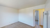 This single-floor residence features a 1-bedroom, 1-bathroom layout designed for functional and efficient living. The interior presents a clean, minimalist aesthetic with smooth white walls and neutral-toned carpeting that runs throughout the living areas, creating a bright and cohesive atmosphere. The open feel of the main living space is enhanced by simple, uncluttered lines and a well-proportioned layout that maximizes the available floor area. A wide doorway connects the primary living area to an adjoining room, allowing for an easy flow between spaces. The secondary room benefits from natural light provided by a window, adding brightness and a sense of openness to the interior. The smooth, white ceilings complement the light walls, contributing to an airy and welcoming ambiance throughout. The straightforward design of this residence makes it an adaptable space, well-suited for a variety of furnishing arrangements and personal styles. Overall, the unit offers a practical and move-in-ready environment with a calm, neutral palette that serves as an excellent foundation for personalization.