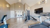 Located at 24 Post Rd in Duxbury, Massachusetts, this fitness center offers a thoughtfully designed single-floor exercise space that combines functionality with an open, airy atmosphere. The room's most striking architectural feature is its dramatic vaulted ceiling, which soars to impressive heights and creates a spacious, energizing environment. Warm neutral-toned walls complement the light wood-look flooring, giving the space a clean and modern aesthetic.

Natural light floods the interior through large arched windows and glass-paneled double doors on both ends of the room, offering views of the surrounding outdoor area. Geometric pendant light fixtures hang from the high ceiling, adding a stylish touch to the practical setting. A wall-mounted flat-screen television provides entertainment during workouts.

The exercise room is well-equipped with a diverse selection of fitness equipment, including treadmills, recumbent and upright stationary bikes, a multi-station cable strength machine, a weight bench, and additional strength equipment. A water cooler station is conveniently positioned near the entrance. The space also features a wall-mounted storage unit, a mini-split HVAC system for climate control, and ample open floor space for stretching or floor exercises, making it a comprehensive and inviting facility for residents.