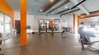 Located at 243 Chicago Ave S in Minneapolis, MN, this fitness center is a comprehensively outfitted facility designed to support a wide range of workout routines. The space is organized across a single floor and divided into distinct functional zones, each thoughtfully equipped for different training disciplines.

The main strength training area features rubber flooring, large wall-to-wall mirrors that amplify the sense of space, and a robust selection of equipment including cable machines, a multi-function strength station, adjustable benches, and multiple dumbbell racks. Bold orange accent walls and columns punctuate the otherwise neutral white and gray palette, lending the space an energetic, modern atmosphere. Exposed ductwork runs along the ceiling, contributing to an industrial aesthetic while recessed lighting ensures the area is well lit throughout.

The cardio zone is lined with large windows that allow natural light to pour in, and includes a row of treadmills, stationary bikes, and stair climbers, all equipped with individual monitors.

A separate studio room features light hardwood flooring, floor-to-ceiling mirrors, and a clean, open layout ideal for stretching, yoga, or cycling. An adjoining room with rubber flooring provides space for functional training and houses kettlebells, medicine balls, and stability balls. A wall-mounted flat-screen television adds a modern convenience to the training environment.
