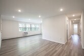 Located at 500 Peconic St in Ronkonkoma, New York, this single-floor unit has been thoughtfully updated throughout, offering a clean, modern aesthetic with a bright and airy atmosphere. The open living area is anchored by light-toned hardwood-style flooring and recessed lighting, with large windows that invite abundant natural light and offer views of the surrounding greenery. A baseboard heating system and wall-mounted AC unit ensure year-round comfort. The galley-style kitchen is well-appointed with white shaker cabinetry, light countertops, and a full suite of stainless steel appliances including a gas range, microwave, dishwasher, and refrigerator. A hallway connects the living spaces to the private quarters, where carpeted bedrooms provide a softer, quieter environment. One bedroom features a spacious closet with double hanging rods. The bathroom is finished with tile flooring, a tub-shower combination with sliding glass doors, a white vanity, and clean white wall tile. An additional versatile room with warm hardwood-style flooring and a built-in niche offers flexible use as a home office or bonus space. The unit combines functional design with fresh finishes throughout.