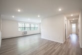 Located at 500 Peconic St in Ronkonkoma, New York, this single-floor unit has been thoughtfully updated throughout, offering a clean, modern aesthetic with a bright and airy atmosphere. The open living area is anchored by light-toned hardwood-style flooring and recessed lighting, with large windows that invite abundant natural light and offer views of the surrounding greenery. A baseboard heating system and wall-mounted AC unit ensure year-round comfort. The galley-style kitchen is well-appointed with white shaker cabinetry, light countertops, and a full suite of stainless steel appliances including a gas range, microwave, dishwasher, and refrigerator. A hallway connects the living spaces to the private quarters, where carpeted bedrooms provide a softer, quieter environment. One bedroom features a spacious closet with double hanging rods. The bathroom is finished with tile flooring, a tub-shower combination with sliding glass doors, a white vanity, and clean white wall tile. An additional versatile room with warm hardwood-style flooring and a built-in niche offers flexible use as a home office or bonus space. The unit combines functional design with fresh finishes throughout.