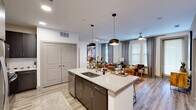 This thoughtfully designed 2-bedroom, 3-bathroom residence offers a seamless open-concept layout that maximizes its single-floor footprint. The kitchen serves as the centerpiece, featuring a large granite-topped island with a double sink, dark espresso cabinetry, stainless steel appliances, and a classic subway tile backsplash. Pendant lighting and track lighting above the island provide both task illumination and visual appeal, while the open flow leads directly into the living and dining areas. The living room is bright and inviting, benefiting from multiple large windows dressed with floor-length drapes that bring in generous natural light. Both bedrooms are carpeted and generously sized, each equipped with a ceiling fan and ample natural light from well-positioned windows. The primary bedroom includes a spacious walk-in closet with built-in shelving and hanging systems for organized storage. The bathrooms are elegantly finished, with one featuring a soaking tub surrounded by large-format stone-look tile and another offering a double-sink vanity with granite countertops, dark cabinetry, a glass-enclosed shower, and stylish geometric flooring. Light wood-look flooring runs throughout the main living areas, tying the modern aesthetic together cohesively.
