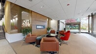 Located at 20 Kelly Ave in Akron, Ohio, this large-scale commercial facility offers a thoughtfully designed, single-floor layout encompassing a generous amount of space. The entrance welcomes visitors with terrazzo flooring, floor-to-ceiling glass panels, and views of the surrounding streetscape, setting a professional tone from the moment of arrival.

The main lobby features a striking wood-paneled accent wall with a linear fireplace, complemented by rich leather seating in warm cognac and bold red tones, arranged over a patterned area rug — creating a polished yet inviting atmosphere. Adjacent common areas showcase an industrial-modern aesthetic, with exposed ductwork and dark ceilings contrasted by vibrant orange accent walls, large pendant lighting, and expansive window walls that flood the space with natural light.

A spacious common corridor connects key areas including a cafeteria-style market with an illuminated service counter, open dining seating, and decorative slatted partitions. Conference rooms are well-appointed with large wall-mounted displays, whiteboards, built-in cabinetry, and signature orange accent walls. A transitional atrium area features glass-railed staircases with wood handrails and curated artwork. Signage throughout references amenities including elevators, a fitness center, and a golf simulator.