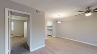 This single-story space presents a clean, functional layout with a cohesive neutral color scheme and light wood-look flooring spanning the main living areas. The open living and dining area is connected by a passthrough view into the kitchen, with a pendant light fixture anchoring the dining space. A textured ceiling adds subtle dimension throughout.

The galley-style kitchen is well-appointed, featuring white shaker cabinetry, granite-look countertops, a subway tile backsplash, a double stainless steel sink, and black appliances including a range and dishwasher. A window above the rear door allows natural light to brighten the space.

The bedrooms offer comfortable proportions, with one featuring plush carpeting and a ceiling fan with light kit, and another finished with the same wood-look flooring found throughout the main areas. Both rooms include closet storage, with louvered and walk-in closet options visible. The bathroom is efficiently designed with a vanity featuring a granite-look countertop, a toilet, and a shower/tub combination. Overall, the unit maintains a practical and well-maintained character throughout.