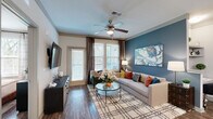Located at 161 Grande Oaks Dr in Charleston, SC, this well-appointed two-bedroom, two-bathroom residence offers a thoughtfully designed single-level floor plan. The open-concept living and kitchen area serves as the heart of the home, anchored by rich hardwood-style flooring that runs throughout. The living room features a bold teal accent wall, ceiling fan, large windows with floor-length drapes, and a door leading to an outdoor balcony, flooding the space with natural light and providing a seamless indoor-outdoor connection. The kitchen is equipped with stainless steel appliances including a range, microwave, dishwasher, and refrigerator, complemented by light wood cabinetry, a tile backsplash, and a granite-topped island with bar seating and a modern pendant light fixture — ideal for both meal prep and casual dining. The primary bedroom is a comfortable retreat with a ceiling fan, natural light from a window, and dedicated closet space. The second bedroom mirrors this warmth with similar finishes and ample storage. Each of the two bathrooms features wood-tone cabinetry, granite countertops, hardwood-style flooring, and a tub-shower combination. Both bedrooms include dedicated closets, adding to the home's practical storage solutions throughout.
