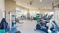 Located at 4009 Harbour Landing Drive in Regina, Saskatchewan, this fitness centre offers a bright and spacious environment designed to support a well-rounded exercise routine. The main workout area features soaring ceilings lined with large, elevated windows on multiple walls, flooding the space with abundant natural light and providing views of the surrounding Harbour Landing community. Ceiling fans and recessed linear lighting contribute to a comfortable and well-lit atmosphere throughout.

The facility is comprehensively equipped with a dedicated cardio zone housing Matrix-brand treadmills, elliptical trainers, and a stationary bike, all positioned alongside floor-to-ceiling windows with a wall-mounted flat-screen TV for entertainment. The strength and free weights area includes a multi-station cable machine, adjustable benches, a full dumbbell rack, and stability balls, complemented by large wall mirrors that enhance the sense of openness. The durable, dual-tone flooring — light grey in the central zone and blue along the perimeter — defines the workout areas clearly.

A private washroom is conveniently accessible from the main floor, featuring wood-look tile flooring, a toilet, and a hand station, providing functional amenities for users. The overall design is clean, modern, and purposefully organized to maximize usability within a generously proportioned single-level layout.