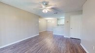 Located at 959 Lake Harbour Dr in Ridgeland, Mississippi, this single-floor residence offers two bedrooms and two bathrooms within a well-organized layout. The open living area features durable wood-look flooring, neutral toned walls, and a ceiling fan with light fixture overhead. A textured ceiling adds subtle character throughout the main living space. The kitchen is equipped with white cabinetry, laminate countertops, a full-size refrigerator, and a peninsula that opens to the adjacent dining area, which is accented by a chandelier. A sliding glass door in the dining area fills the space with natural light and offers a pleasant outdoor view of the surrounding greenery. Both bedrooms are carpeted for comfort, providing a warm contrast to the hard flooring in the common areas. The primary bedroom includes a dedicated walk-in closet outfitted with wire shelving and hanging rods for organized storage. The bathrooms are clean and functional, with one featuring a full tub-shower combination with white tile surround. Additional storage is available via a closet accessible from the main living area. The overall aesthetic is light, neutral, and move-in ready.
