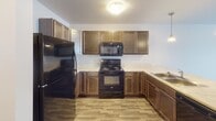 Located at 1233 Tom Sawyer Trail in Harrisburg, South Dakota, this single-floor residence offers a well-organized layout designed for everyday comfort and practicality. The kitchen is a standout feature, equipped with rich dark wood cabinetry, light stone-finish countertops, and a full suite of black Whirlpool appliances including a refrigerator, electric range, over-the-range microwave, and a sink — all set on durable wood-look flooring that flows throughout the functional areas of the home. The full bathroom is thoughtfully appointed with matching dark wood vanity cabinetry, a white countertop with an integrated sink, a large mirror with overhead lighting, a combined tub and shower, and the same warm wood-look flooring, creating a cohesive aesthetic. A dedicated laundry room provides added convenience with a full-size washer and dryer included, along with overhead wire shelving for storage. The bedroom is a calm, neutral space featuring plush carpeting, a window with blinds that invites natural light, and clean white walls. The overall design of the home emphasizes clean lines, neutral tones, and practical finishes, making it a comfortable and move-in ready residence in the growing community of Harrisburg, SD.