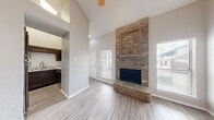 This two-story home is defined by its striking architectural details and functional layout. The living room serves as the centerpiece of the main floor, boasting soaring vaulted ceilings that amplify the sense of space and openness. A dramatic floor-to-ceiling brick fireplace with a raised brick hearth anchors the room, extending upward to create a bold focal point. Light-toned wood-look flooring runs throughout the main living areas, complementing the neutral wall tones and clean white baseboards. Multiple windows dressed with horizontal blinds invite natural light throughout.

Adjacent to the living room, the kitchen is equipped with dark espresso cabinetry, light stone-look countertops, a stainless steel double sink, and stainless steel appliances including an electric range and over-the-range microwave. A classic white subway tile backsplash adds a clean, modern contrast to the dark cabinetry.

Upper-level rooms feature plush carpeting, ceiling fans, and vaulted ceilings. One bedroom includes mirrored sliding closet doors and an interior pass-through window. A full bathroom offers a white tub-shower combination with built-in shelving. Throughout, the home maintains a bright, neutral palette that lends a clean and welcoming ambiance.