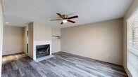 Located at 4045 Treadway Rd in Beaumont, TX, this two-story residence offers a well-organized layout spread across two floors. The main level features a combined dining and living area finished with stylish grey wood-look flooring, a ceiling fan, and a wood-burning fireplace with a white brick surround and built-in mantle shelf — a standout focal point of the space. A staircase with white railing leads to the upper level, while large windows allow natural light to fill the room. The kitchen is conveniently situated on the main floor alongside a pantry and additional closet storage. A pass-through opening connects the kitchen to the adjacent living area, enhancing the open feel of the lower level. Upstairs, the spacious bedroom is finished with plush carpeting, vaulted ceilings, and a ceiling fan. A generously sized walk-in closet with wire shelving provides ample storage. Sliding glass doors open onto a private balcony, offering outdoor space and natural views. The upper level also includes a full bathroom equipped with a grey vanity with granite-style countertop, a large mirror, and hardwood-style flooring. Throughout the home, neutral tones and consistent finishes create a cohesive and inviting atmosphere.