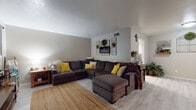 This single-story home offers a well-distributed layout across multiple rooms, each reflecting a distinct personality through thoughtful décor. The living room serves as the heart of the home, featuring light wood-look flooring, neutral painted walls, and a large L-shaped sectional sofa accented with yellow and teal throw pillows. Decorative wall art, trailing greenery, and farmhouse-style signage add warmth and character to the space.

The galley-style kitchen is efficiently designed with white cabinetry lining both sides, dark granite-style countertops, a stainless steel sink, and black appliances, including a range and refrigerator. Light flooring continues throughout, complementing the clean, functional layout.

The bedrooms are carpeted and individually styled. The primary bedroom accommodates a full-sized bed with a tufted bench at the foot, ceiling fan, and curtained windows. A second bedroom features ivy-adorned walls and a crib alongside a bed, functioning as a shared children's room. Additional bedrooms offer ceiling fans and natural light from standard windows.

The bathroom includes a wood-tone vanity with dark countertops, a large mirror, and a shower-tub combination accented by a bold geometric-patterned curtain and rustic open shelving above the toilet.