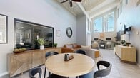 Located at 3114 Terry Brook Drive in Winter Park, FL, this 570-square-foot single-floor space makes a striking architectural impression through its soaring vaulted ceilings with exposed beams and a ceiling fan, creating an open and airy atmosphere throughout. Large, floor-to-ceiling windows along the front wall flood the interior with abundant natural light while offering views of the lush Florida landscape, including a palm tree visible from the main living area.

The living room serves as the centerpiece of the space, featuring light-toned large-format tile flooring that runs throughout. The open layout accommodates distinct functional zones: a seating area with modern furnishings, including a leather sofa and swivel accent chairs, a round dining table with black chairs, and a dedicated workstation along the wall with a long desk and monitor setup. A wall-mounted TV above a natural wood credenza completes the media area.

A hallway connects the main space to the bathroom, which features the same tile flooring, a wood-toned vanity, a full mirror, a wall-mounted grab bar for accessibility, and decorative framed artwork. The overall design palette is clean and contemporary, with white walls, neutral tones, and modern fixtures creating a bright, functional, and welcoming environment.