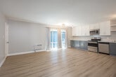 Located at 1821 E Fifth St in Long Beach, California, this 2-bedroom, 1-bathroom unit offers a well-designed single-floor layout with a clean, modern aesthetic throughout. Light wood-style flooring runs continuously through the space, creating a cohesive and bright atmosphere.

The open-concept kitchen and living area forms the heart of the unit. The kitchen is outfitted with stainless steel appliances — including a range, microwave, and dishwasher — complemented by two-tone cabinetry featuring white upper cabinets and slate-blue lower cabinets, all topped with white countertops. A pantry provides additional storage, and the space flows naturally into the living area, which receives natural light through sliding glass doors draped with neutral curtains.

Both bedrooms are comfortably sized, with the primary bedroom offering a window with outdoor views. Each bedroom includes ceiling fans and wall-unit air conditioning for year-round comfort, as well as closet space with built-in shelving and hanging rods. The second bedroom also features an open closet area.

The bathroom is finished with vertical white subway tile surrounding a tub-shower combination, a sleek vanity with a white countertop, and wood-look flooring, giving it a fresh, contemporary feel. A hallway connects the rooms efficiently, rounding out this well-appointed unit.