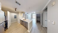 Located at 3850 W Northwest Hwy in Dallas, TX, this two-story, 3-bedroom, 3-bathroom residence offers a well-designed layout spread across two floors. The main level, which comprises the majority of the living space, features an open-concept kitchen and living area anchored by a large kitchen island with a white quartz countertop, a black matte faucet, and a built-in sink. White cabinetry pairs with stainless steel appliances, including a refrigerator, gas range, and microwave. Light wood-style flooring runs throughout the main level, complementing the neutral gray tones of the walls and crown molding details. A dramatic floor-to-ceiling window bathes the living area in natural light, while a sleek staircase with black metal railings leads to the upper level. Soaring ceilings with a modern ceiling fan add to the sense of volume in the main living space. The spacious primary bedroom is carpeted and includes a private en-suite bathroom and a walk-in closet with wire shelving. Bathrooms feature tiled shower-tub combos with brushed nickel fixtures. Additional highlights include a dedicated in-unit laundry area with a top-load washer, multiple closets for ample storage, and a hallway layout that promotes privacy between bedrooms.