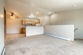 This two-floor residential space offers a functional and practical layout designed for comfortable everyday living. The main living area is open and spacious, featuring neutral-toned carpet, vaulted ceilings, and a ceiling fan that enhances airflow throughout. Baseboard heating runs along the walls, providing efficient warmth. The kitchen is well-equipped with warm oak cabinetry, light countertops, white appliances including a range and refrigerator, and tile-style flooring. A half-wall peninsula separates the kitchen from the living space, creating an open yet defined layout that encourages easy interaction between areas. A full bathroom includes an oak vanity with a light countertop, a tub-shower combination, and tile flooring. Additional rooms include a carpeted bedroom with a window that allows natural light to filter in, accompanied by baseboard heating. The space also features an attached single-car garage with an automatic opener, offering direct access and added convenience. Throughout the home, oak wood trim and warm neutral tones create a cohesive and understated aesthetic. The overall layout is straightforward and well-organized, making it a practical and move-in ready space.