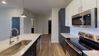 Located at 15927 White St in Charlotte, NC, this single-floor residence presents a clean, contemporary design characterized by neutral gray tones, wood-style luxury vinyl plank flooring throughout the main living areas, and an open, functional layout.

The living area is spacious and well-lit, benefiting from natural light through windows fitted with horizontal blinds. Recessed lighting adds an additional layer of brightness, and a door provides direct access to the outdoors, enhancing connectivity with the exterior environment.

The kitchen is a standout feature, designed with dark lower cabinetry contrasted by white upper cabinets, granite-look countertops, and stainless steel appliances including a refrigerator, microwave, and range. A central island with a deep stainless steel sink and pendant lighting above creates a practical and visually appealing focal point. The layout is well-organized, offering ample counter and storage space.

The bedroom features plush carpeting, a ceiling fan with integrated lighting, and a window allowing natural light. A walk-in closet provides generous storage. The bathroom is equipped with a granite-topped vanity with dark cabinetry, a tub-shower combination with tiled surround, and consistent wood-style flooring, completing the cohesive design of the home.